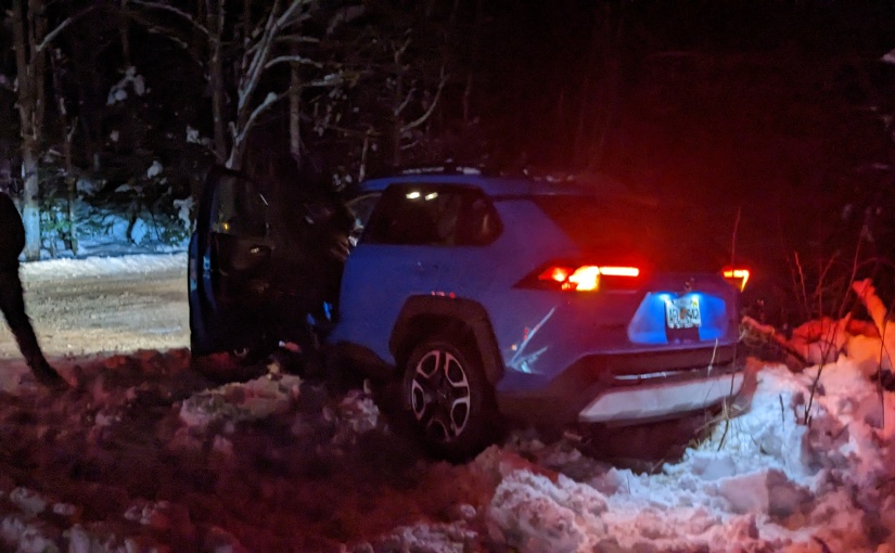 A blue Rav 4 stuck in a snow bank and leaning at a precarious angle