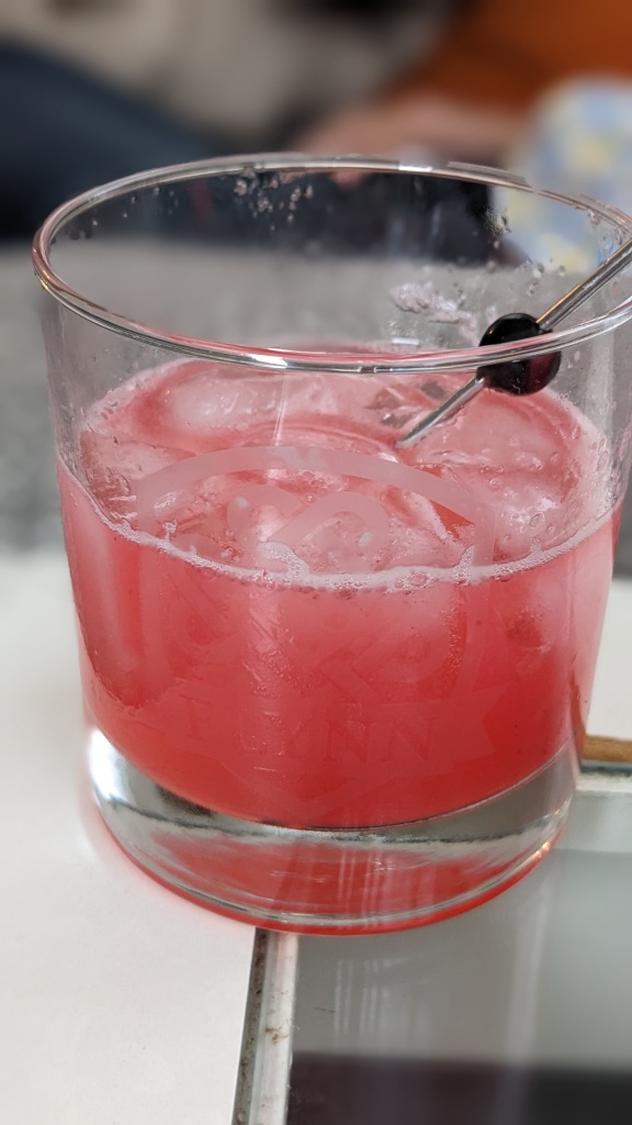 A lowball glass filled with a pink drink and with a speared berry as decoration